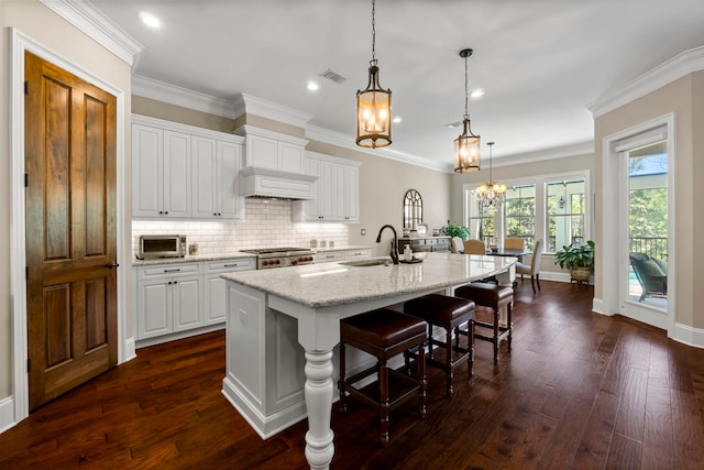 kitchen featuring white cabinetry, dark hardwood / wood-style flooring, a chandelier, an island with sink, and light stone countertops