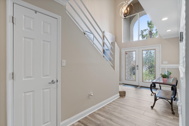 foyer entrance featuring french doors, crown molding, light hardwood / wood-style floors, and a notable chandelier