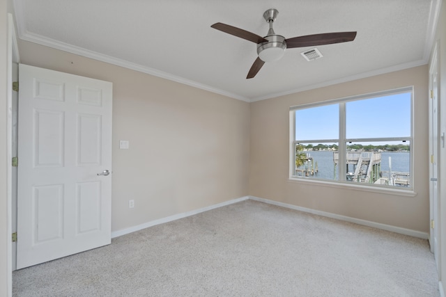 carpeted spare room with ornamental molding, ceiling fan, and a water view