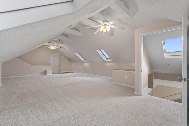 bonus room featuring light carpet, lofted ceiling with skylight, ceiling fan, and a textured ceiling