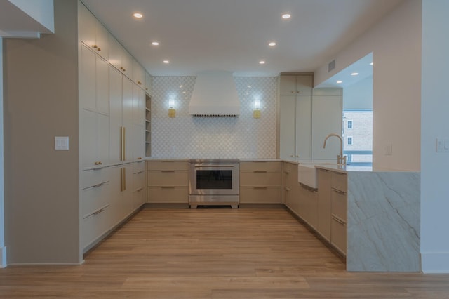 kitchen with oven, custom exhaust hood, sink, and light wood-type flooring