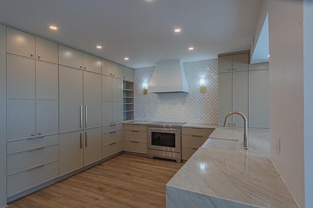 kitchen featuring custom exhaust hood, stainless steel range, sink, light stone counters, and light hardwood / wood-style floors