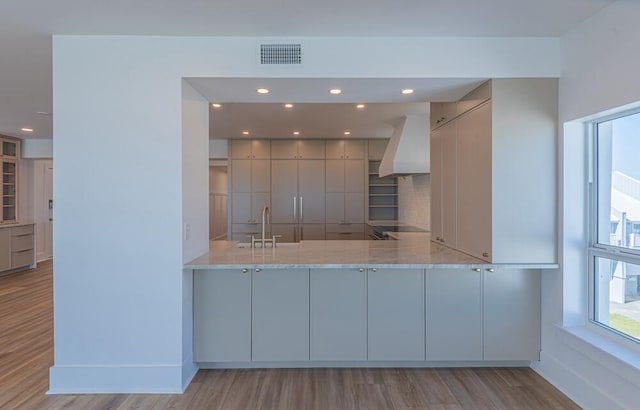 kitchen with custom range hood, light hardwood / wood-style floors, and light stone counters