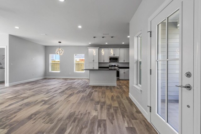 kitchen featuring white cabinets, stainless steel appliances, hanging light fixtures, and wood-type flooring