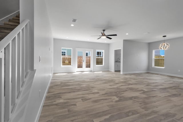 unfurnished living room featuring french doors, light wood-type flooring, and ceiling fan with notable chandelier