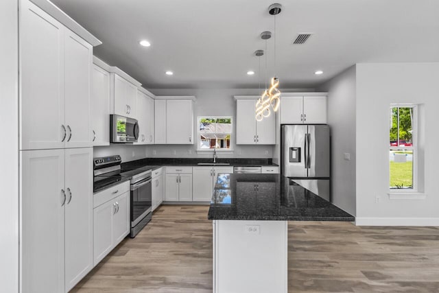 kitchen featuring white cabinetry, appliances with stainless steel finishes, decorative light fixtures, and a center island