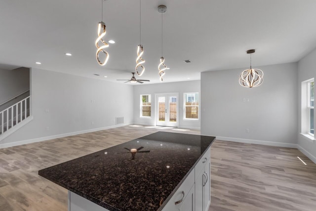 kitchen with dark stone counters, light hardwood / wood-style flooring, a kitchen island, white cabinets, and pendant lighting