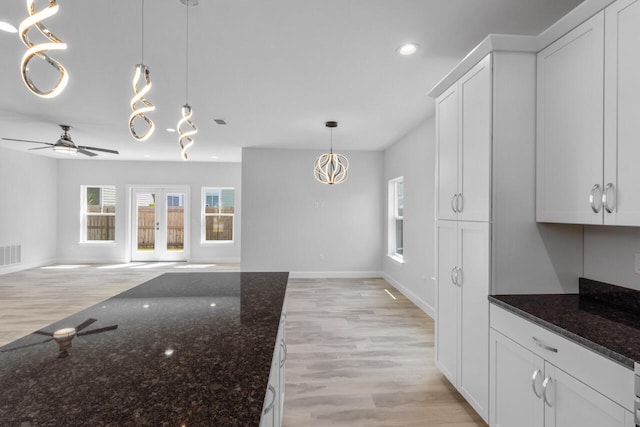 kitchen featuring dark stone countertops, pendant lighting, white cabinets, and light hardwood / wood-style flooring