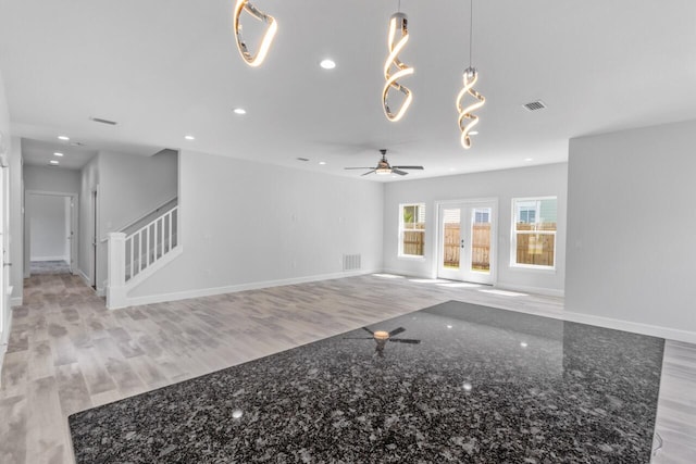 unfurnished living room featuring french doors, ceiling fan with notable chandelier, and light hardwood / wood-style flooring