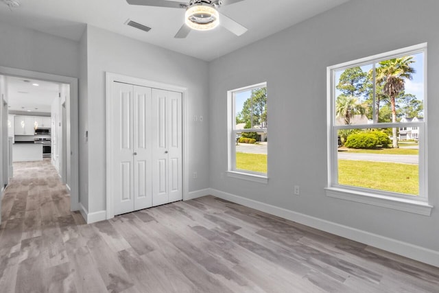 unfurnished bedroom featuring light hardwood / wood-style floors, ceiling fan, multiple windows, and a closet