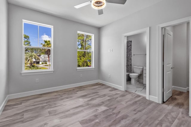 unfurnished bedroom with ceiling fan, ensuite bath, and light wood-type flooring