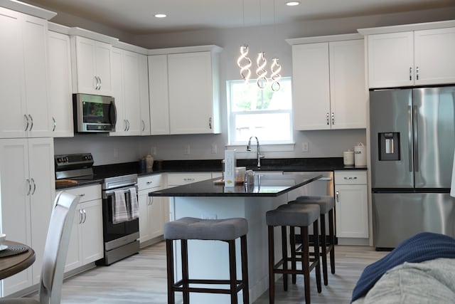 kitchen with a kitchen island, white cabinetry, appliances with stainless steel finishes, a breakfast bar area, and light hardwood / wood-style flooring