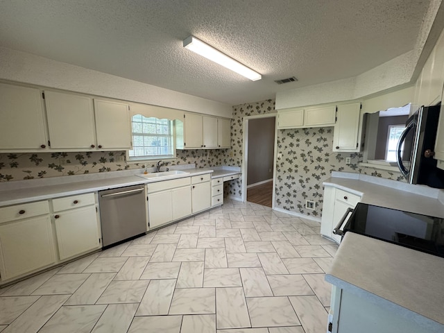 kitchen featuring sink, a textured ceiling, light tile floors, and stainless steel dishwasher