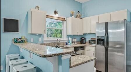 kitchen featuring appliances with stainless steel finishes, white cabinets, a breakfast bar area, kitchen peninsula, and light stone countertops