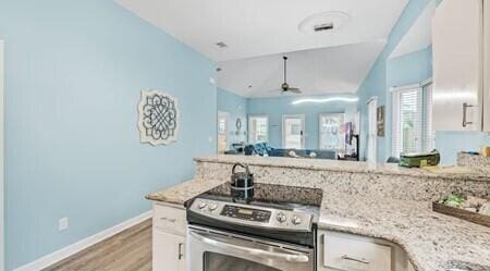 kitchen featuring light stone countertops, light hardwood / wood-style flooring, white cabinetry, stainless steel range with electric cooktop, and ceiling fan