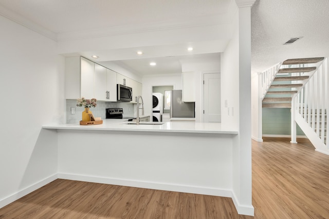 kitchen with appliances with stainless steel finishes, light hardwood / wood-style floors, stacked washer and dryer, tasteful backsplash, and white cabinetry