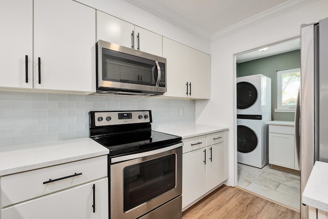 kitchen with light tile floors, tasteful backsplash, white cabinetry, stacked washing maching and dryer, and stainless steel appliances