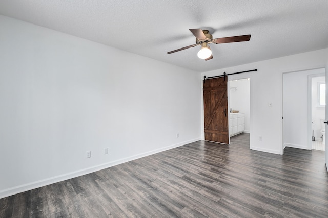 unfurnished bedroom with connected bathroom, dark hardwood / wood-style floors, a barn door, ceiling fan, and a textured ceiling