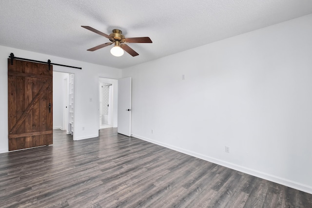 unfurnished bedroom with a barn door, dark wood-type flooring, ceiling fan, and a textured ceiling