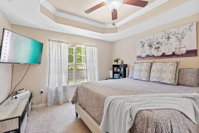 carpeted bedroom with ceiling fan, a tray ceiling, and ornamental molding