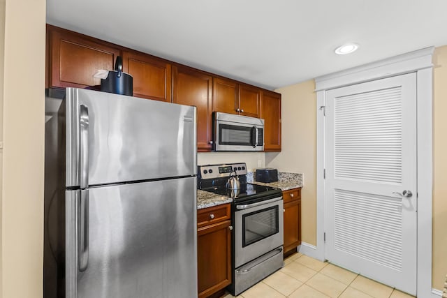 kitchen with stainless steel appliances, light tile floors, and light stone counters