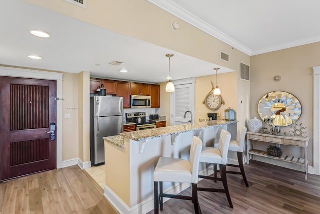 kitchen with light stone counters, appliances with stainless steel finishes, light wood-type flooring, hanging light fixtures, and kitchen peninsula