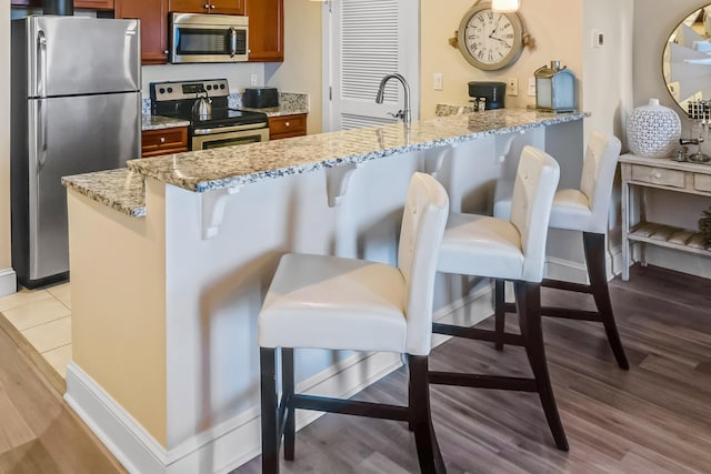 kitchen featuring appliances with stainless steel finishes, a breakfast bar area, and light stone counters