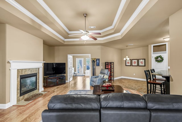 living room with light wood-type flooring, ceiling fan with notable chandelier, french doors, a tray ceiling, and ornamental molding