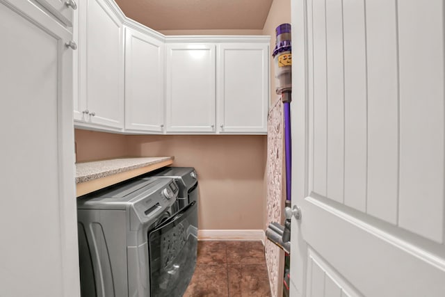 washroom featuring washing machine and dryer, dark tile floors, and cabinets