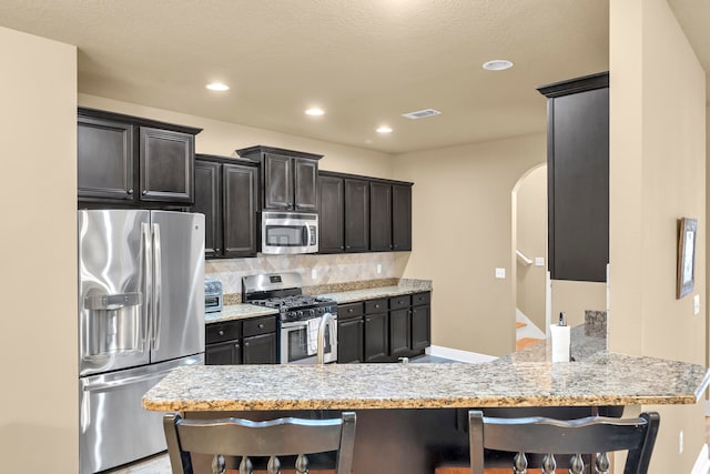 kitchen with appliances with stainless steel finishes, tasteful backsplash, kitchen peninsula, a kitchen breakfast bar, and light stone countertops