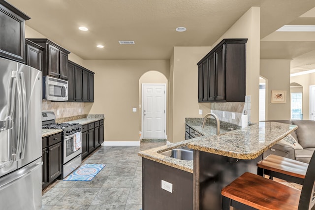 kitchen with kitchen peninsula, appliances with stainless steel finishes, backsplash, light tile flooring, and a kitchen breakfast bar