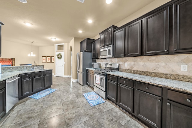 kitchen with light stone countertops, decorative light fixtures, appliances with stainless steel finishes, backsplash, and light tile floors