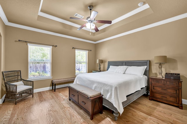 bedroom featuring a raised ceiling, crown molding, and light wood-type flooring