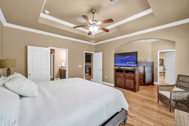 bedroom featuring light hardwood / wood-style flooring, connected bathroom, ceiling fan, and a tray ceiling