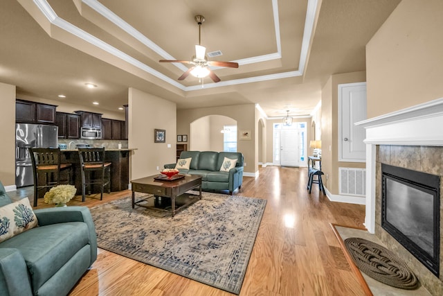 living room with a fireplace, a raised ceiling, ceiling fan, and light hardwood / wood-style flooring