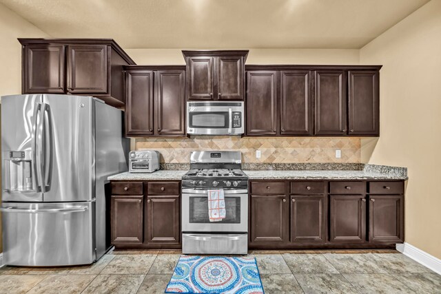 kitchen with dark brown cabinetry, light stone counters, light tile floors, tasteful backsplash, and stainless steel appliances