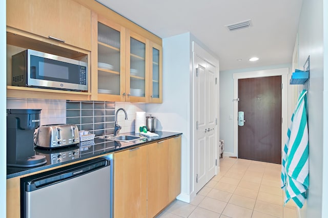 kitchen with appliances with stainless steel finishes, light brown cabinetry, sink, light tile flooring, and tasteful backsplash