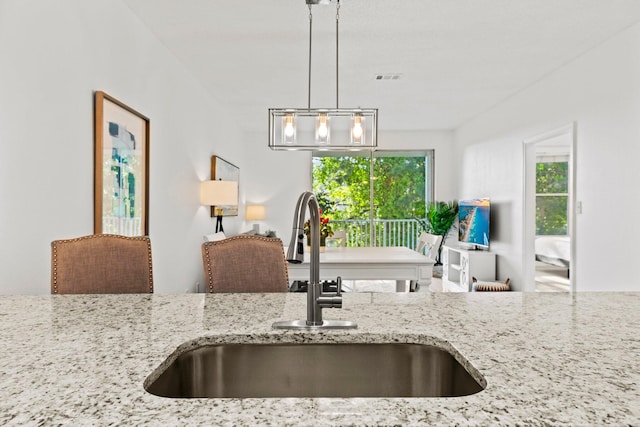 kitchen with hanging light fixtures, sink, and light stone counters