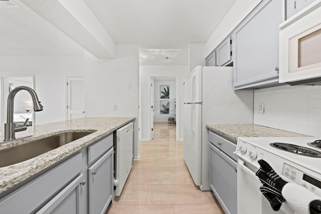 kitchen with light tile floors, sink, white appliances, tasteful backsplash, and light stone countertops