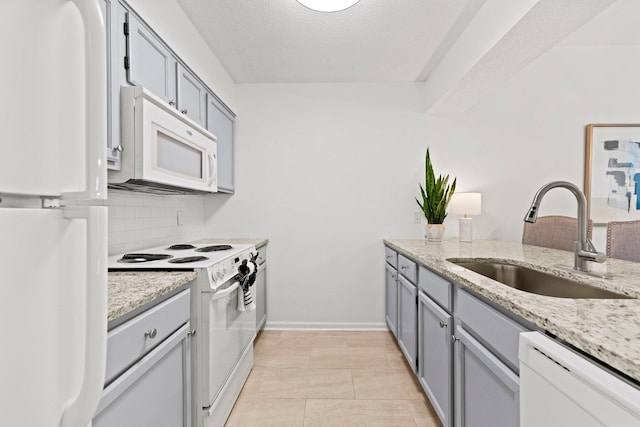 kitchen with white appliances, tasteful backsplash, light stone countertops, and sink