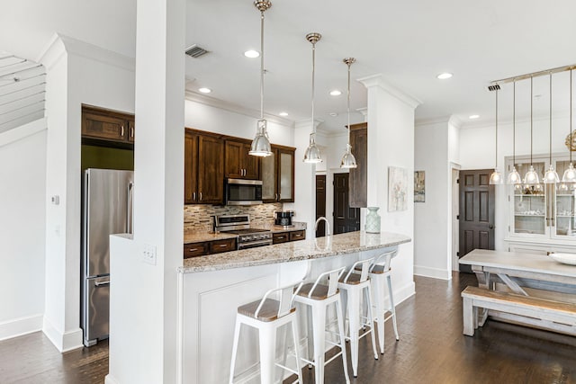 kitchen featuring pendant lighting, dark hardwood / wood-style floors, appliances with stainless steel finishes, light stone counters, and tasteful backsplash