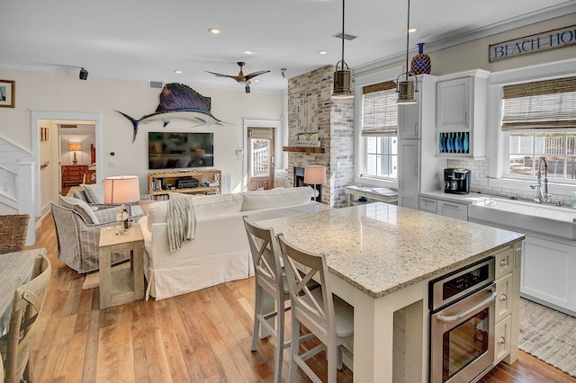 kitchen with oven, white cabinets, a fireplace, a kitchen island, and light hardwood / wood-style floors