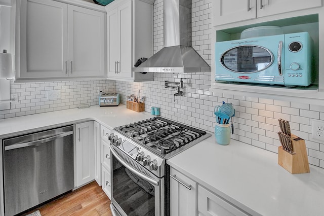 kitchen with gas stove, light hardwood / wood-style floors, wall chimney range hood, white cabinetry, and stainless steel dishwasher