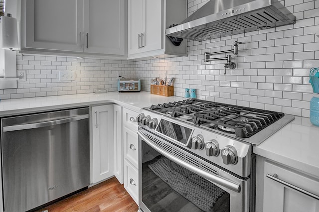 kitchen with appliances with stainless steel finishes, tasteful backsplash, wall chimney range hood, and light wood-type flooring