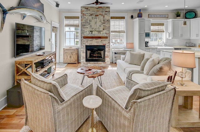 living room with crown molding, light wood-type flooring, sink, and a fireplace