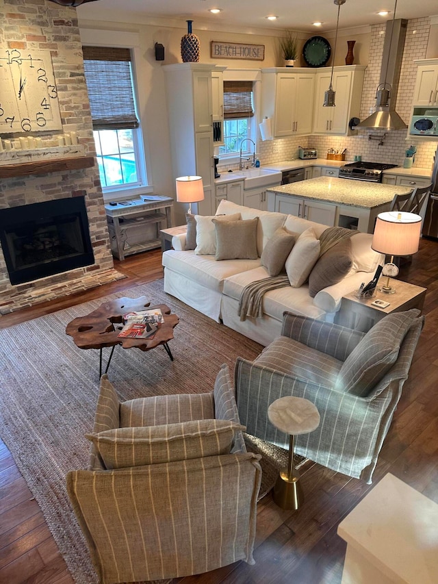 living room featuring ornamental molding, sink, a stone fireplace, and dark wood-type flooring