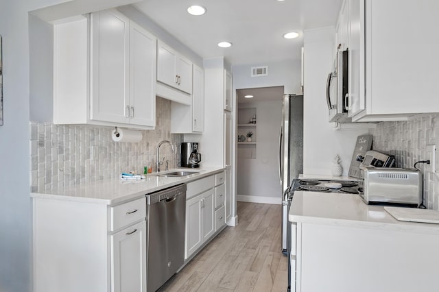 kitchen featuring tasteful backsplash, light wood-type flooring, sink, white cabinets, and appliances with stainless steel finishes