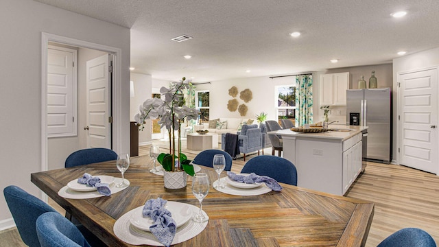 dining room featuring light wood-type flooring, a textured ceiling, and sink