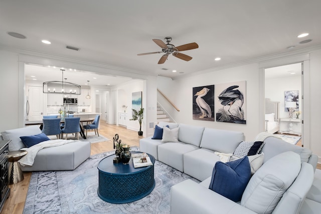 living room with crown molding, light hardwood / wood-style flooring, and ceiling fan with notable chandelier