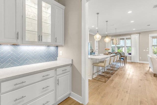 kitchen with hanging light fixtures, decorative backsplash, white cabinets, and light hardwood / wood-style flooring